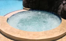 A concrete made inground hot tub filled with water and working jets.