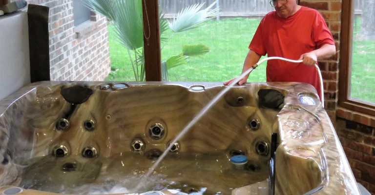 a man filing a hot tub with a garden house pipe after cleaning it