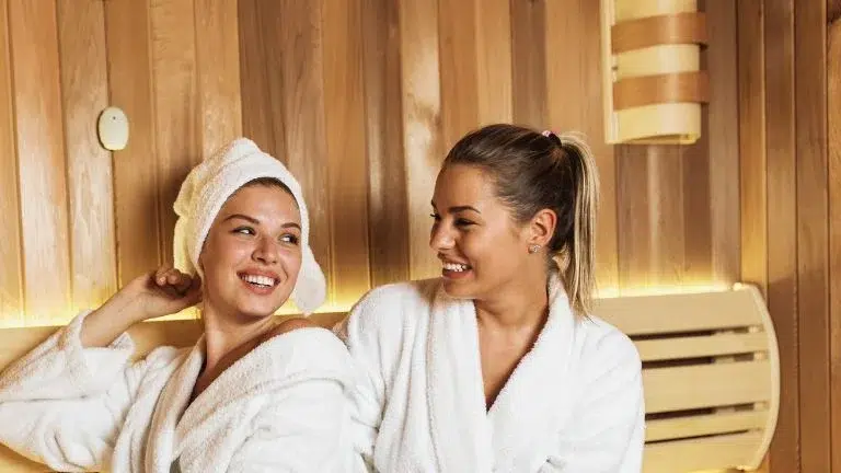 Two individuals relaxing in a wooden sauna, enjoying the Benefits of Sauna for Skin of the warm environment.