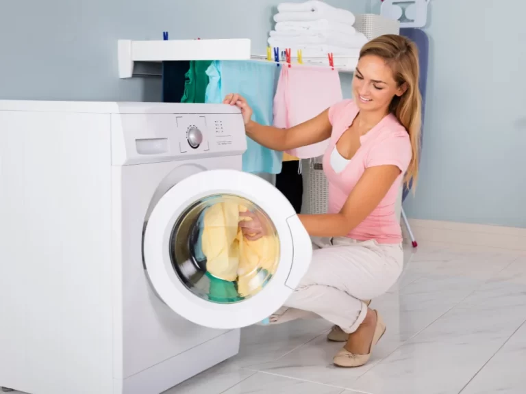 A person loading a yellow item into a white washing machine with a round door.