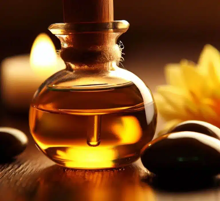 A close-up image of a transparent glass bottle containing a golden liquid, possibly oil, with smooth stones and a yellow flower in the background.