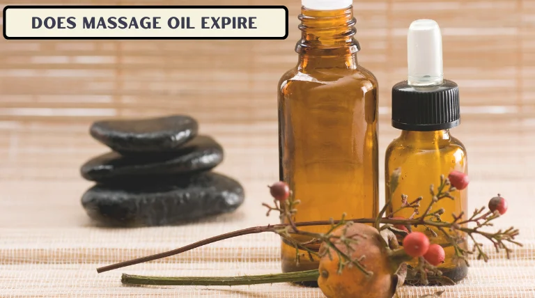 Two amber-colored glass bottles of massage oil, one with a dropper, placed beside a stack of black stones and dried plants with berries on a woven surface.