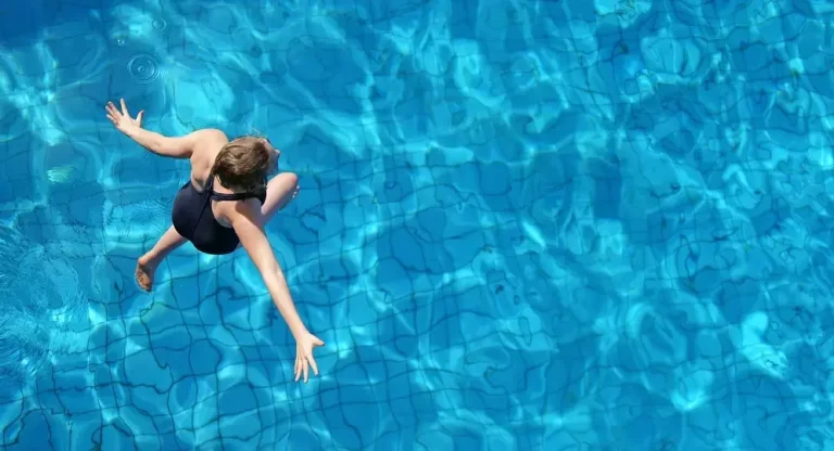 A woman in a black swimsuit diving headfirst into a bright blue swimming pool.