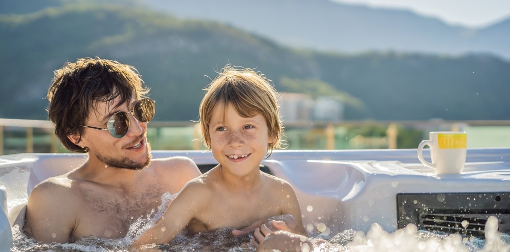 A man wearing black sunglasses with his son soaking in a well-maintained hot tub