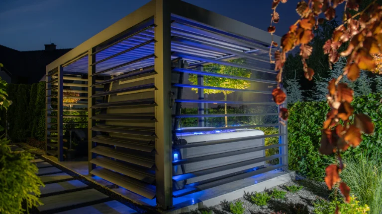 A wooden structure with a hot tub inside, surrounded by plants and trees at night.