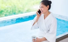 A young woman wearing a white robe holds a cup of coffee, preparing to use the hot tub in the morning.