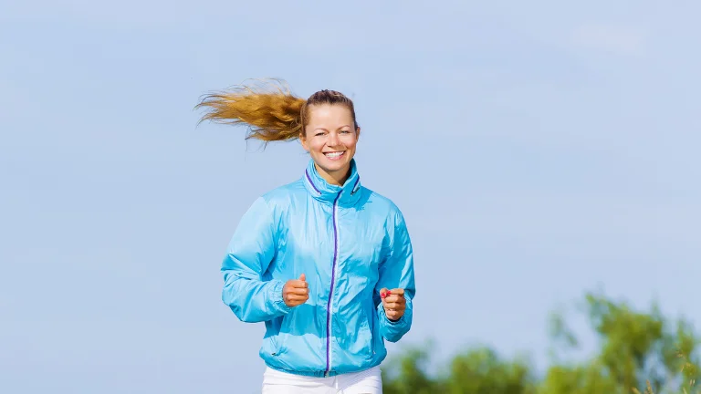 A young woman wearing a blue Sauna Suit jogging on a walking track. (How To Use A Sauna Suit To Cut Weight)