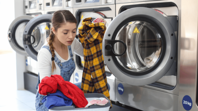 A woman putting a yellow and black checkered shirt into a white washing machine with a yellow triangle on the door.(How To Wash A Sauna Suit)