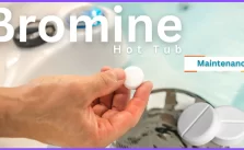 A hand holding a white tablet over a hot tub, with the text “Bromine Hot Tub Maintenance” on the image.