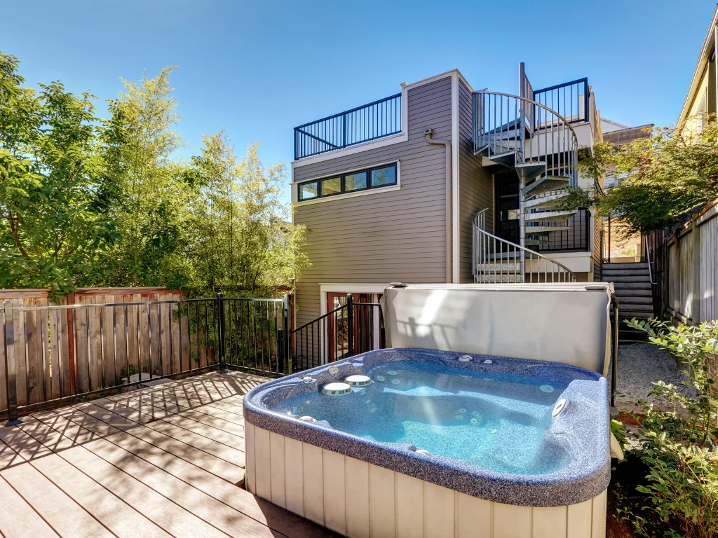 A traditional hot tub on a wooden deck in a backyard.