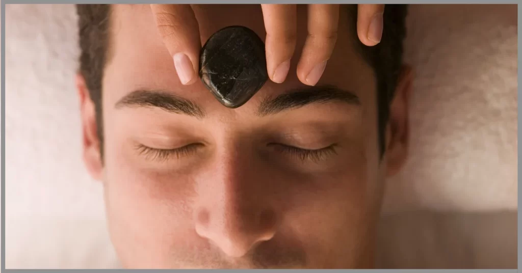 A man taking hand stone massage on her forehead