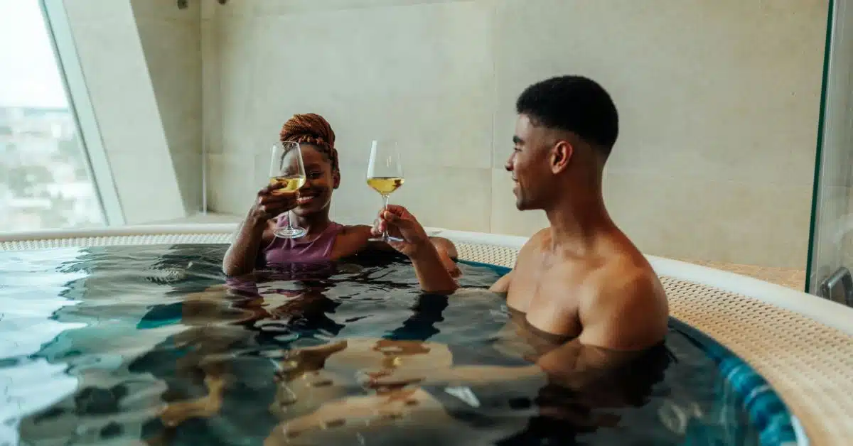 Two young individuals, a male and a female, enjoying a hot tub soak while holding glasses of drinks