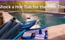 A blue hot tub with a fountain and a pool in the background, surrounded by pool cleaning equipment and a stone wall.