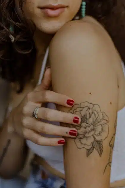 A person’s arm with a black and white flower tattoo and red nails.