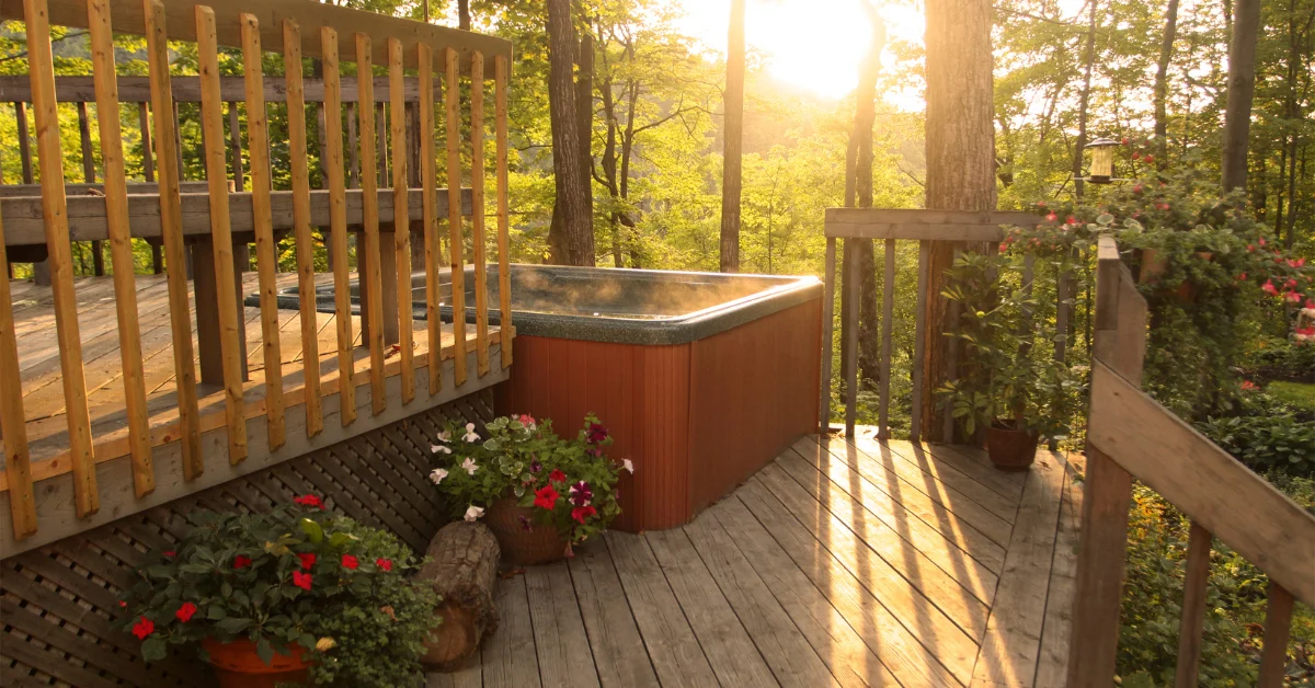  A wooden deck with a hot tub and potted plants in a forested area. (Can I Put a Hot Tub on My Patio)