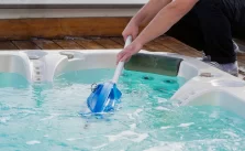 A man cleaning and refilling a blue water hot tub.