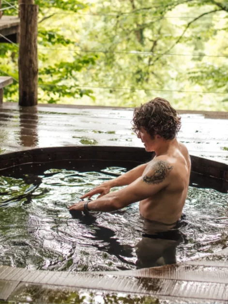 A man holding dumbbells in a wooden hot tub surrounded by trees. (Hot Tub Workout Routines )