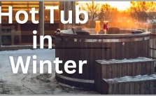 A wooden hot tub on a snowy deck with a sunset view and two glasses of beer.