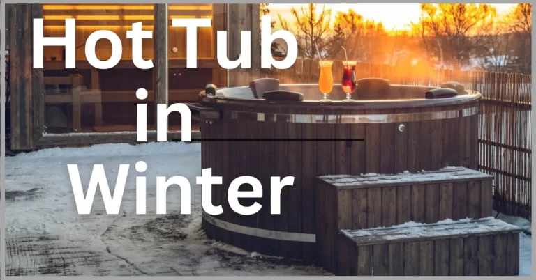 A wooden hot tub on a snowy deck with a sunset view and two glasses of beer.