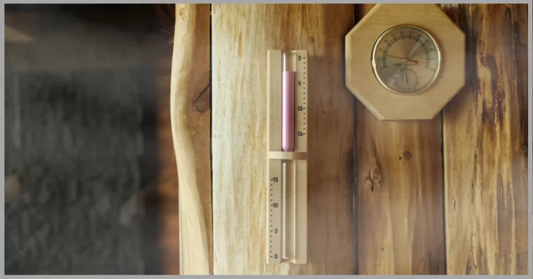 A pink sand timer and a round thermometer on a wooden wall in a steamy sauna.