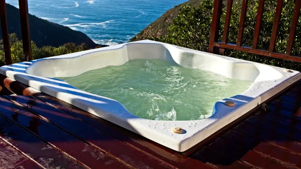 A white hot tub with green water on a wooden deck overlooking the ocean. (Hot Tub Water is Green)