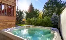 A Hot Tub Water is Green in a backyard with trees and a wooden deck.