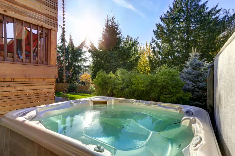 A Hot Tub Water is Green in a backyard with trees and a wooden deck.