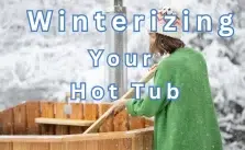 A person in a green robe and a winter hat cleaning a wooden hot tub in a snowy forest.