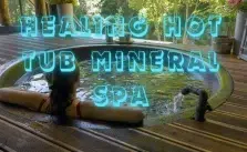 A woman relaxing in a hot tub with the words “healing hot tub mineral spa” in blue neon letters above her.