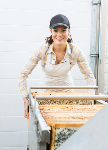 a woman beekeeper smiling face working on a honey extractor