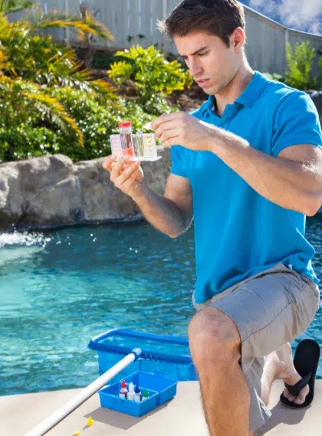 A man wearing blue shirt with a water testing stip checking pool water alkalinity.