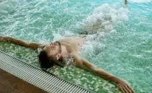 A person relaxing in a hot tub with their arms extended along the pool’s edge. (Arthritis Hot Tubs)