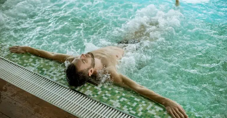 A person relaxing in a hot tub with their arms extended along the pool’s edge. (Arthritis Hot Tubs)