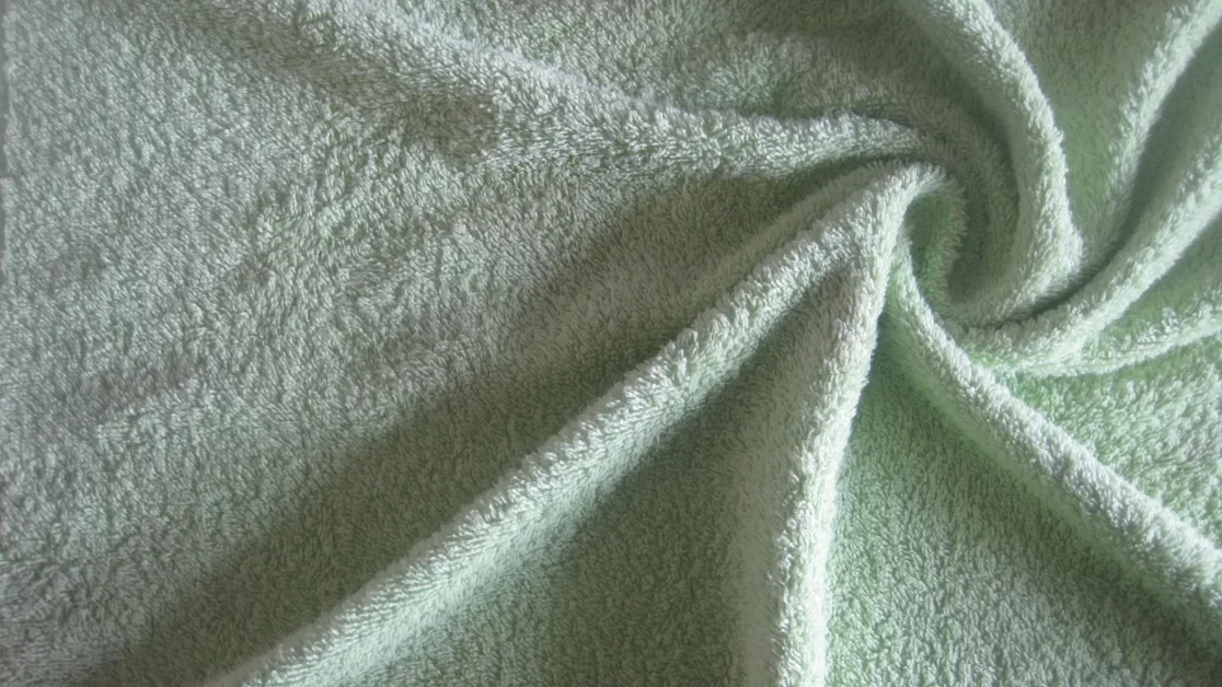 A close-up image of a light green terry cloth fabric, showcasing its soft and absorbent texture.