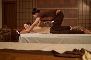 A practitioner performing traditional Eastern massage using foot pressure on a client’s back.