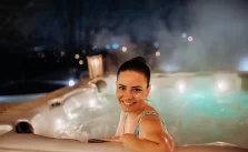 A young woman smiling while enjoying an outdoor bathtub on her terrace, surrounded by greenery.