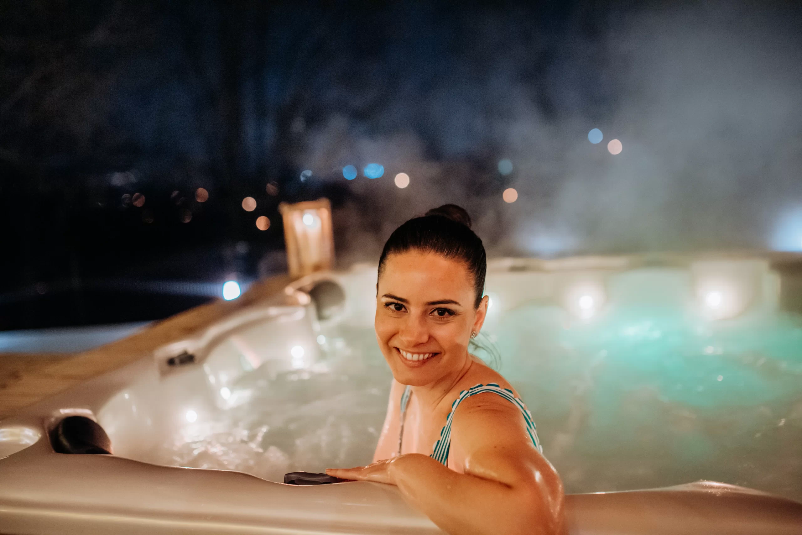 A young woman smiling while enjoying an outdoor bathtub on her terrace, surrounded by greenery.