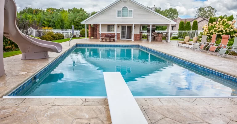 A rectangular plunge pool with clear blue water is situated in a backyard setting, featuring a diving board on one end and a curved slide on the other.