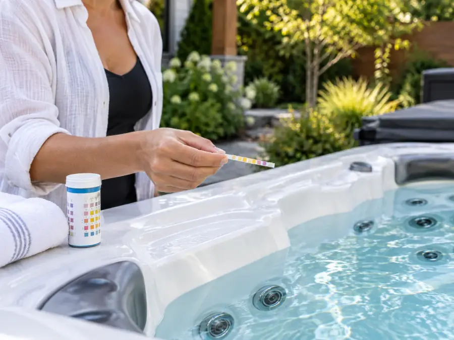Hand checking a water test strip beside an outdoor hot tub